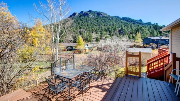A deck with a table and chairs overlooking a mountainous landscape with houses in the background. - Lakeshore Retreat- Estes Park Escape with Mountain & Pond Views (Estes Park)
