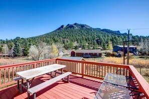 Une terrasse en bois avec une table de pique-nique et des chaises en métal, offrant une vue sur une montagne boisée et des immeubles résidentiels.