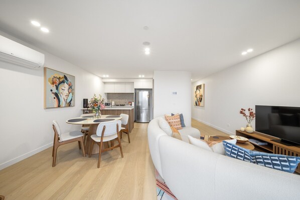 A modern living room with a sofa, TV, and dining area. - Sleek Inner-city 2-bed With Swimming Pool & BBQ (Canberra)