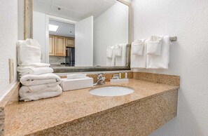 A bathroom with a granite countertop, a white sink, a mirror, and a stack of white towels.