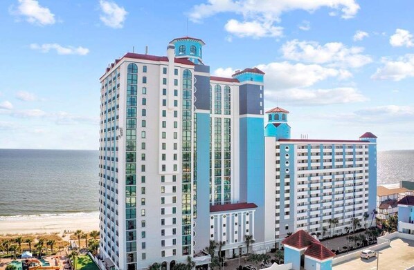 A multi-story hotel with a beach view, featuring a prominent tower and a large building with balconies.