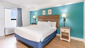 A hotel room with a large bed, two bedside tables with lamps, a view through a window, and a teal accent wall. - Caribbean 1020 (Myrtle Beach)