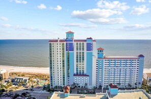 A high-rise hotel with multiple floors, a prominent tower, and a beach view.