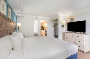 A hotel room with a bed, a television, a dresser, and a view of the kitchen.