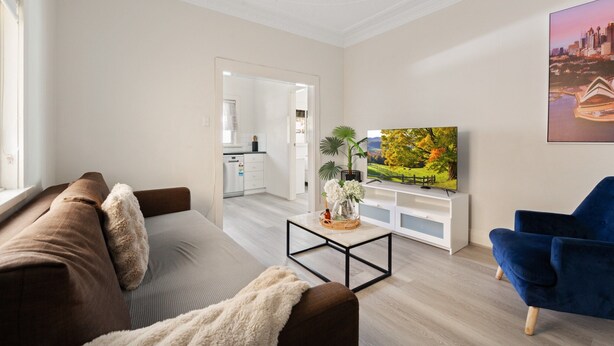 Ett modernt vardagsrum med en brun soffa, en blå fåtölj, ett soffbord och en tv med platt skärm.