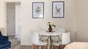 En matplats med ett runt bord, vita stolar och en vas med blommor. På väggen hänger inramade botaniska illustrationer.
