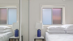 Ett hotellrum med en säng, ett nattduksbord med en lampa och en spegel som reflekterar rummet.