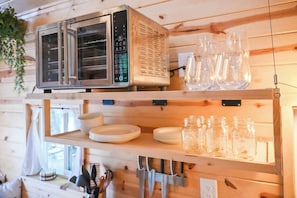 Een keuken met een magnetron, planken met borden en potten, en hangend keukengerei.