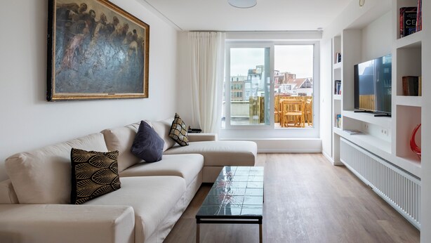 Een moderne woonkamer met een bank, een salontafel, een schilderij en een televisie op een witte dressoir.