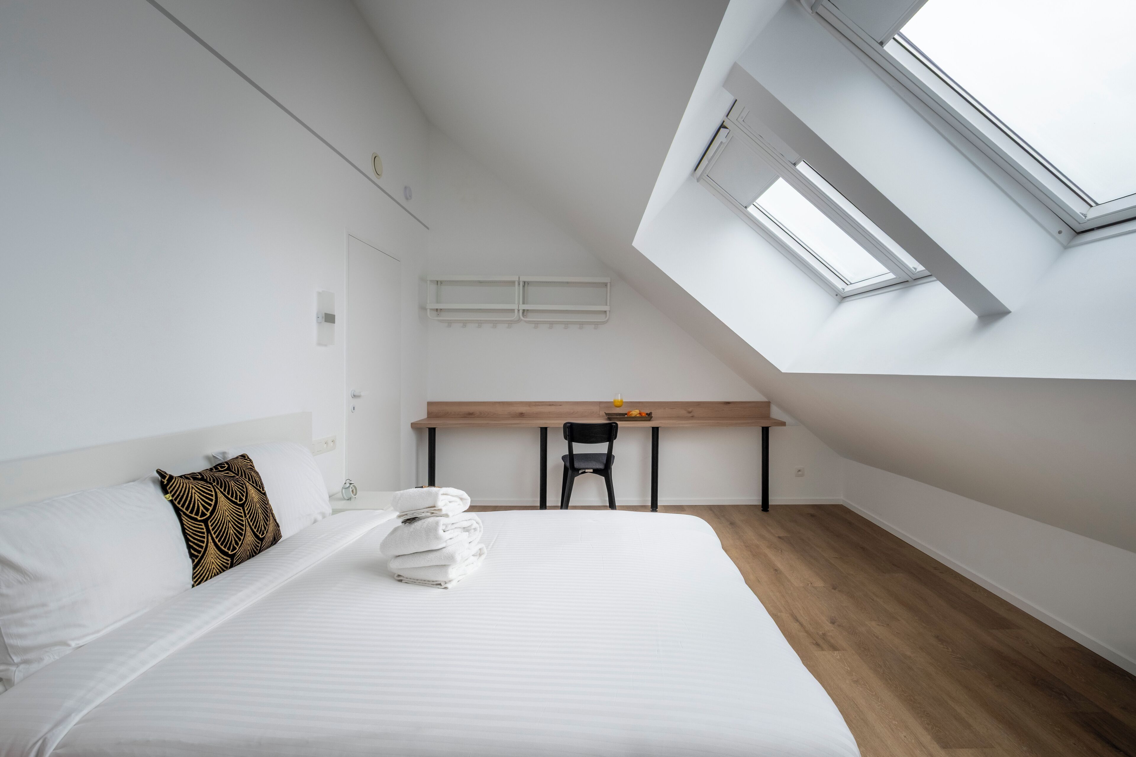 Ein modernes, helles Schlafzimmer mit einem großen Bett, einem Schreibtisch und einem Dachfenster.