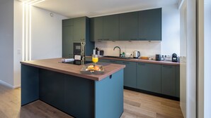 Een moderne keuken met een centraal eiland, donkergroene kastjes en houten vloeren.