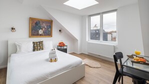 Een moderne slaapkamer met dakraam, een bed met witte lakens, een schilderij aan de muur en een ontbijttray op de tafel.
