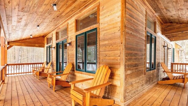Eine Holzhütte mit einer Veranda, Holzstühlen und großen Fenstern.