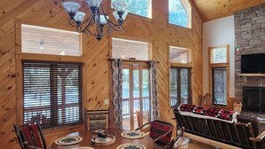 Eine geräumige Holzhütte mit einem großen Esstisch, zahlreichen Fenstern und einem Kamin aus Stein.