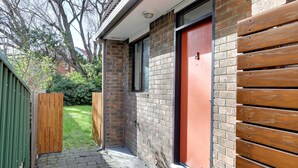 A narrow brick pathway leading to a red door, flanked by wooden fences and a green metal fence. - 2-bed Townhouse Retreat in Sandy Bay With Parking (Hobart)