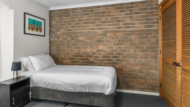 A bedroom with a brick wall, a bed, a nightstand, a lamp, and a wooden door. - 2-bed Townhouse Retreat in Sandy Bay With Parking (Hobart)