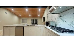 A modern kitchen with white cabinets, a built-in dishwasher, and a stove. - 3-bedroom house near Disneyland in Anaheim with AC (Anaheim)