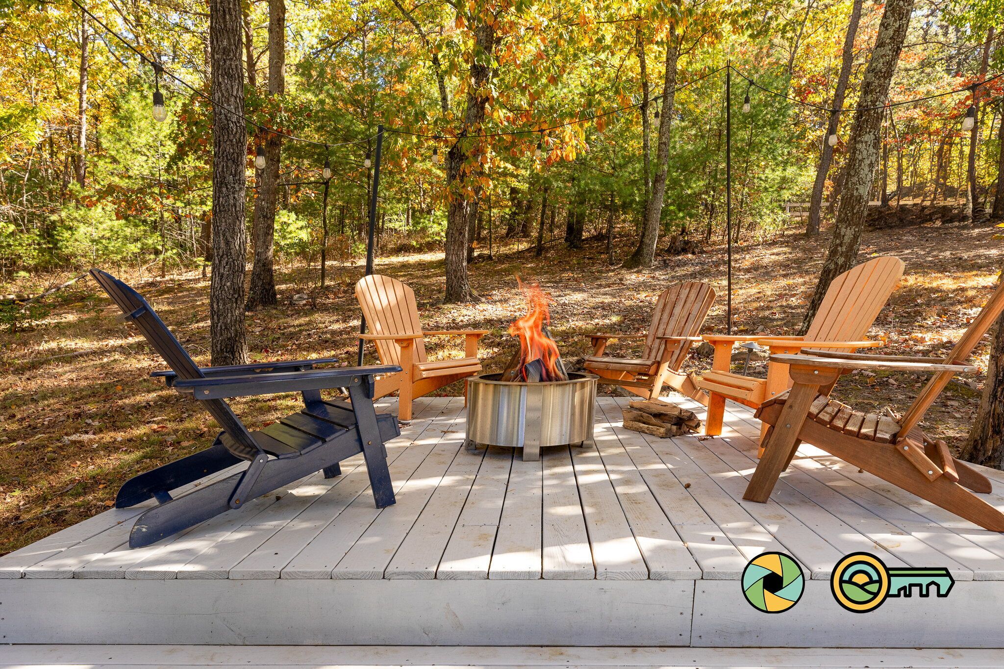 Een terras met Adirondack-stoelen en een vuurkorf in het midden, omringd door een bos.