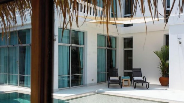 Un área de piscina moderna al aire libre con agua azul cristalina, ventanas amplias y dos sillones de descanso.