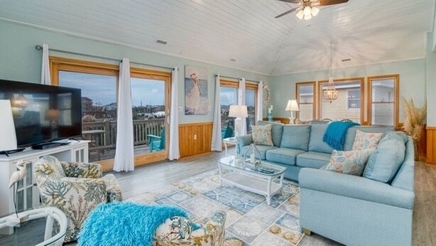 A spacious living room with a large television, a sofa, a coffee table, and a view of the city through large windows. - 1 Minute Walk To The Beach. Spectacular Ocean Views, Sun Rises, & Sun Sets! (Avon)