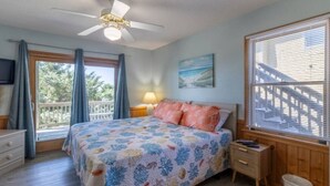 A bedroom with a bed, a ceiling fan, a window with blinds, a nightstand, and a TV on the wall. - 1 Minute Walk To The Beach. Spectacular Ocean Views, Sun Rises, & Sun Sets! (Avon)