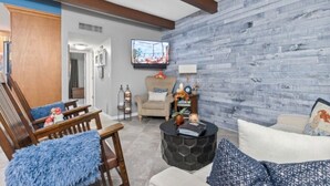 A living room with a wooden floor, a stone coffee table, and a television mounted on the wall.