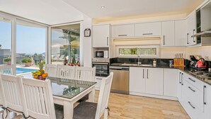A modern kitchen with white cabinets, a dining area with a glass table, and a view of the outdoors.