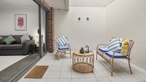 A modern living room with a sofa, two wicker chairs, a small round table, and a glass door leading to a balcony.