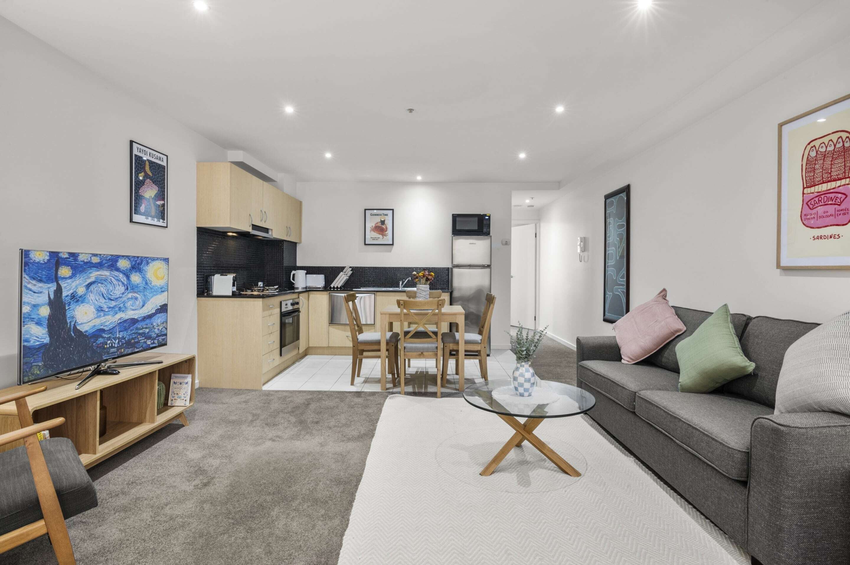 A modern living room with a dining area, kitchen, and a flat-screen TV.