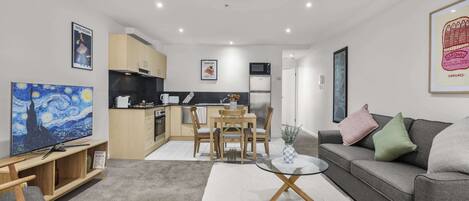 A modern living room with a dining area, kitchen, and a flat-screen TV.