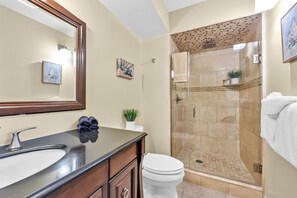 A bathroom with a large mirror, a sink, a toilet, and a glass-enclosed shower area.