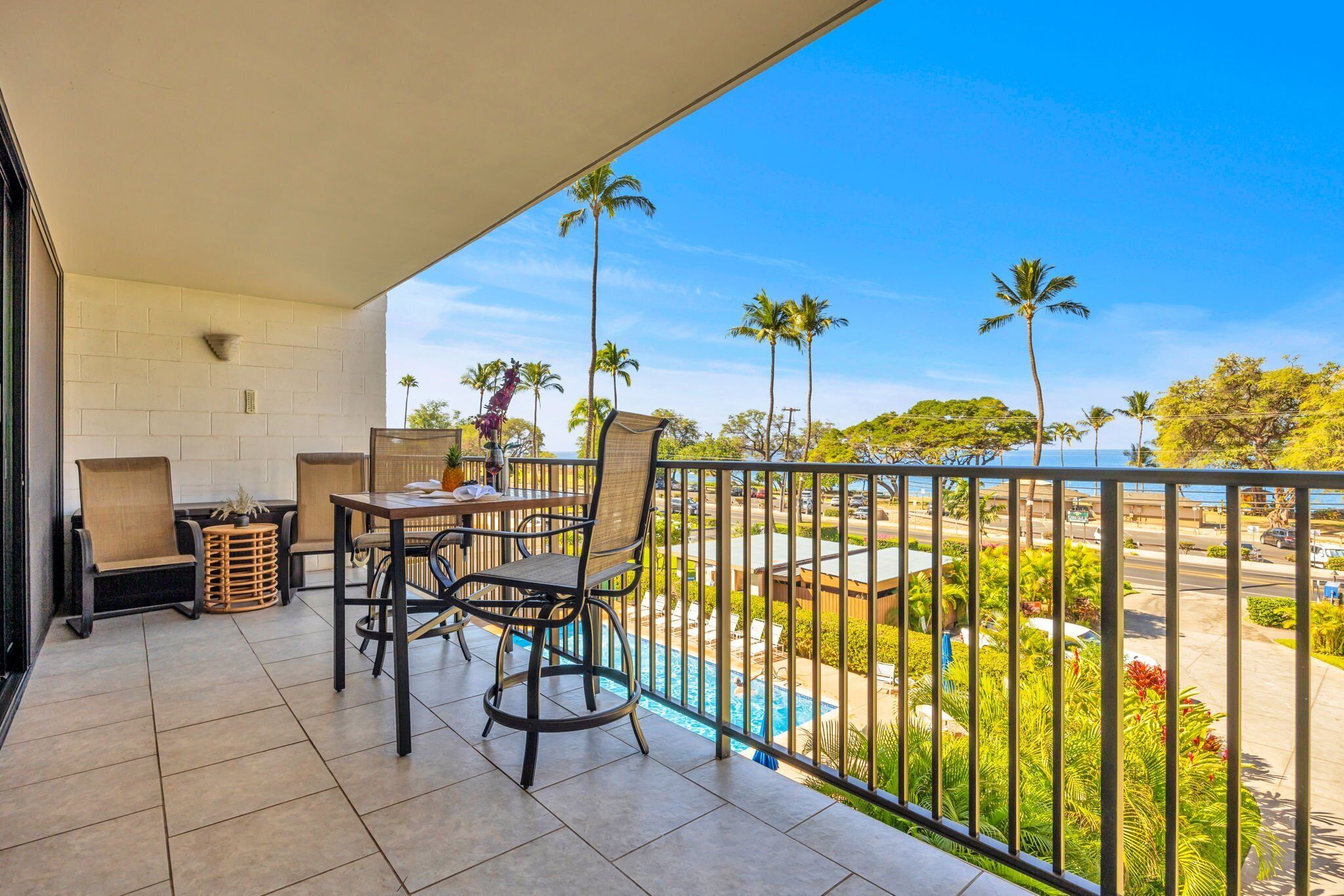 Uma varanda com mesa e cadeiras, com vista para uma piscina e palmeiras.