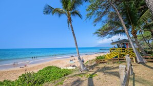Ein Strand mit Palmen, einem Rettungsturm und einem sandigen Ufer mit Menschen.