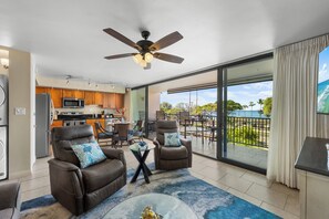 A spacious living area with a view of the ocean, a ceiling fan, and a kitchen in the background.