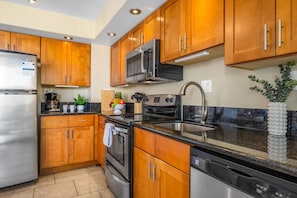 A modern kitchen with wooden cabinets, stainless steel appliances, and a granite countertop. - Recently updated oceanview retreat (Kihei)