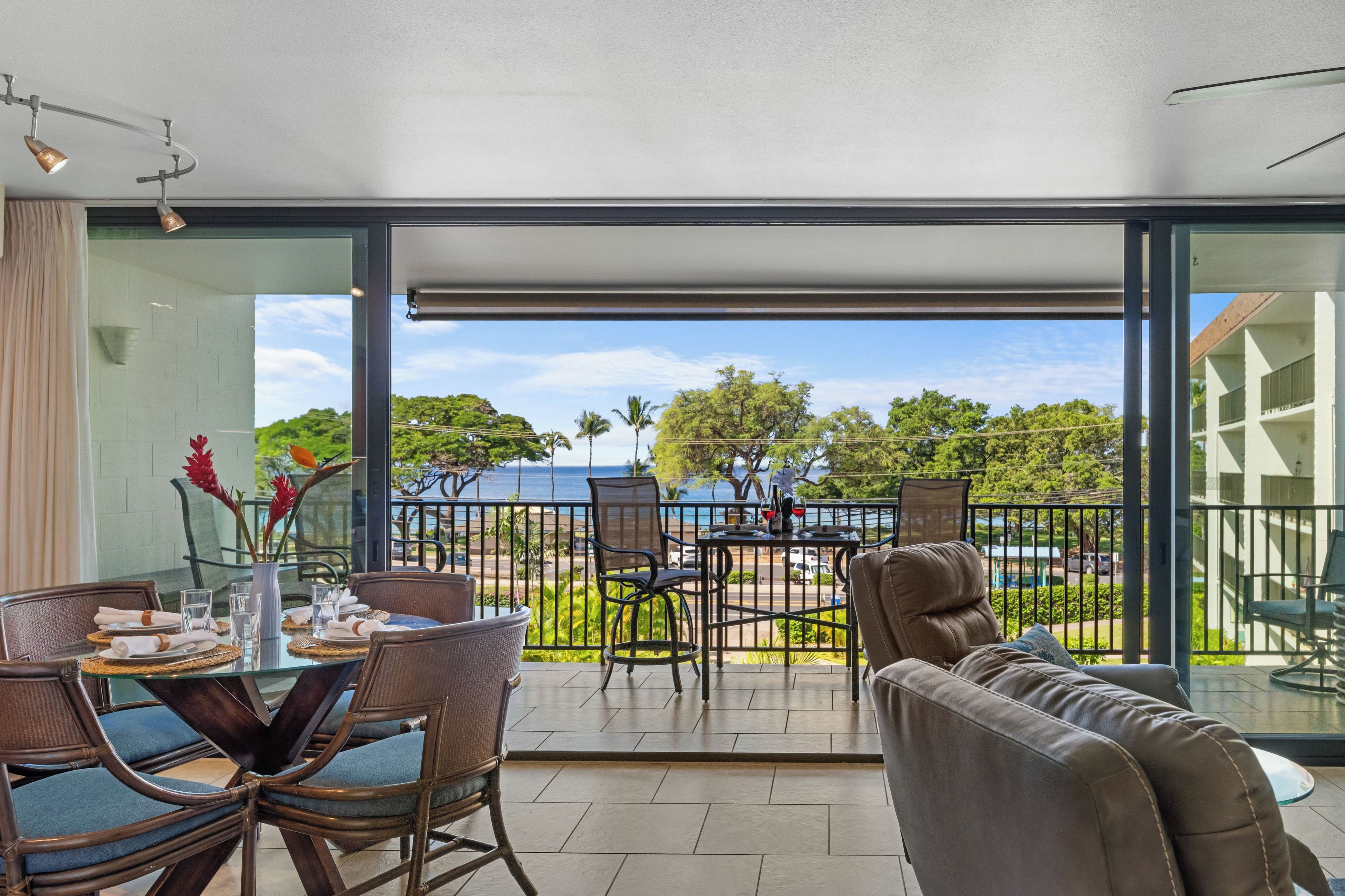 A dining area with a table set for two, overlooking a scenic view of the sea and greenery.