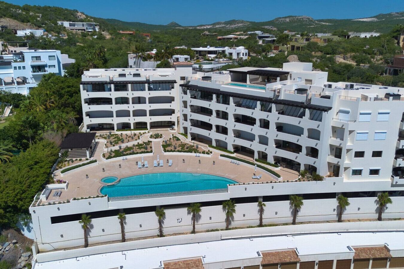 A modern hotel with multiple floors, a central courtyard with a swimming pool, and a landscaped area with palm trees.