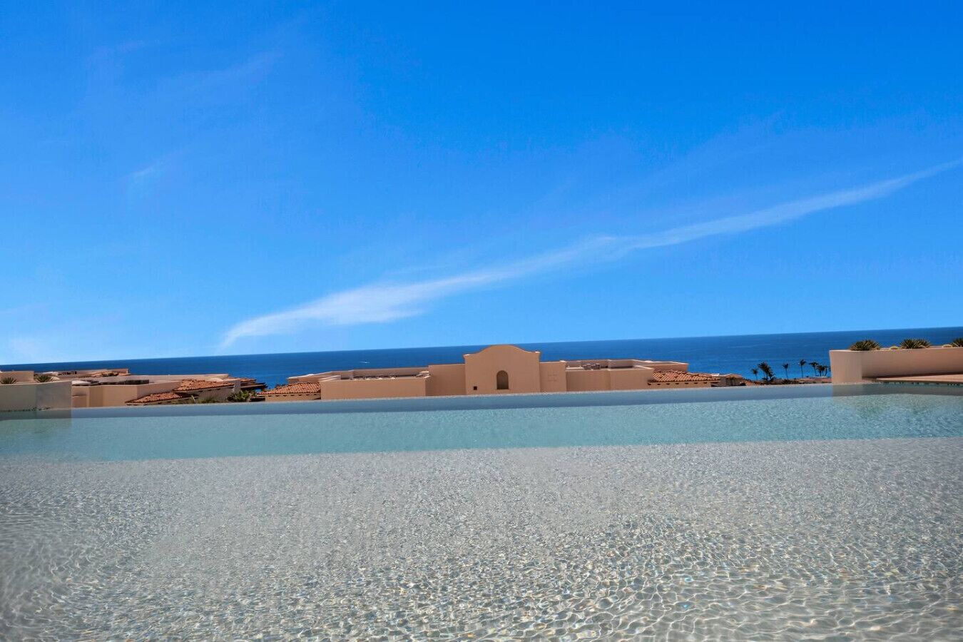 Piscina cristalina con vistas al océano y edificios al fondo.