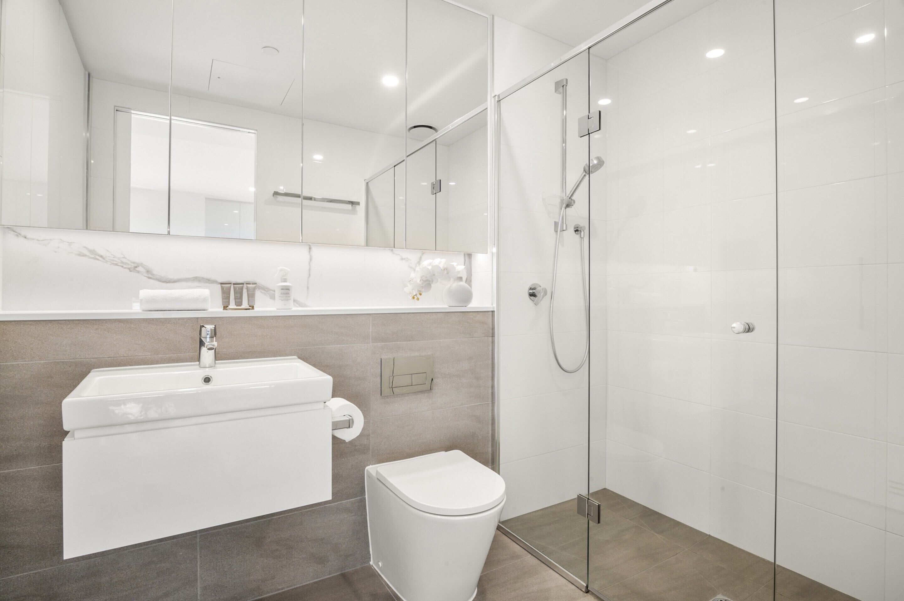 A modern bathroom with a glass-enclosed shower, a white sink, and a toilet.