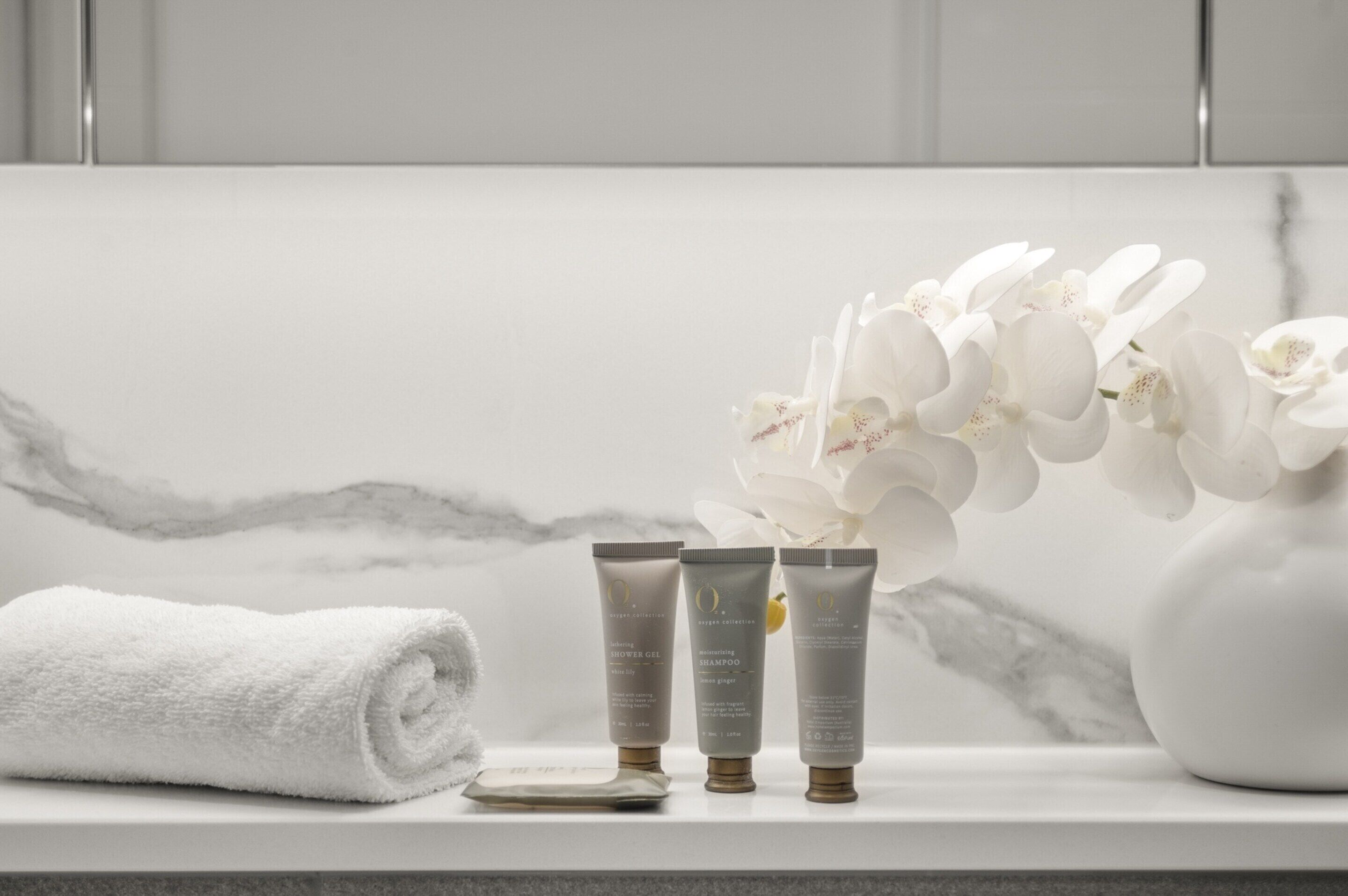 Ein Badezimmer mit Marmorwand, einem weißen Handtuch und drei Flaschen Shampoo und Conditioner.