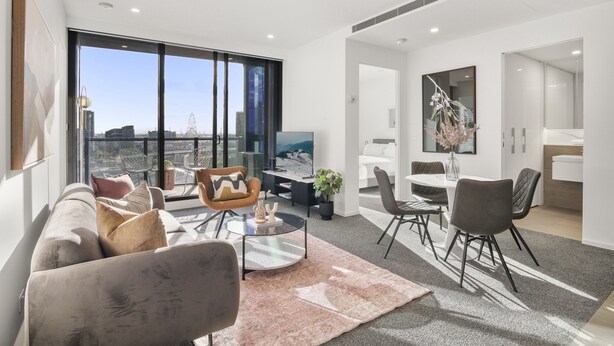 A modern living room with a sofa, coffee table, and chairs, a dining area with a table and chairs, and a large window offering a city view. - Elegant 2-bed With Superb Views & Amenities (Melbourne)