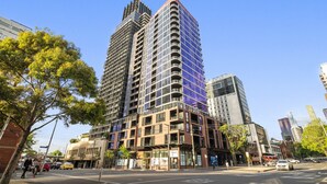 A modern high-rise building with multiple floors, large windows, and a prominent corner design. - Elegant 2-bed With Superb Views & Amenities (Melbourne)