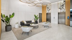 A modern lobby with a sofa, two armchairs, a coffee table, and potted plants. - Elegant 2-bed With Superb Views & Amenities (Melbourne)