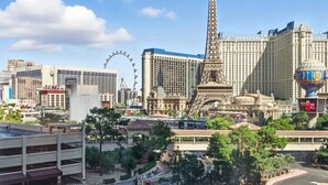 A cityscape with the Eiffel Tower, a Ferris wheel, and a large casino building. - SVS: Designer Tropical 1BD | Bellagio Fountain View | Resort Pool | Jockey Club (Las Vegas)