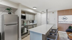 A modern kitchen with stainless steel appliances, a central island, and bar stools. - SVS: Designer Tropical 1BD | Bellagio Fountain View | Resort Pool | Jockey Club (Las Vegas)