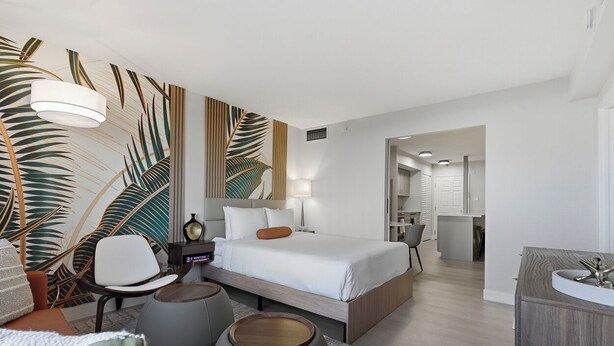 A modern hotel room with a large bed, a desk, and a seating area with ottomans. - SVS: Designer Tropical 1BD | Bellagio Fountain View | Resort Pool | Jockey Club (Las Vegas)