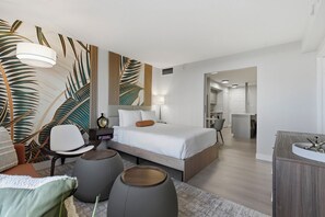 A modern hotel room with a large bed, a desk, and a seating area with ottomans. - SVS: Designer Tropical 1BD | Bellagio Fountain View | Resort Pool | Jockey Club (Las Vegas)