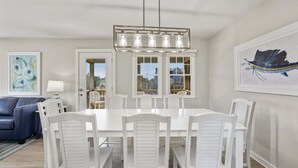 Een eetgedeelte met een witte tafel en stoelen, een hanglamp en kunstwerken aan de muren.