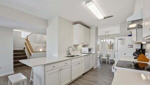 Een moderne keuken met witte kasten, een ingebouwde magnetron en een eethoek met witte stoelen.