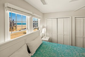 Une chambre à coucher avec un lit, une table de chevet, une lampe et une vue sur la plage par la fenêtre.